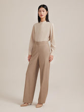 A lady wears a beige colored shirt and a wide leg pants.